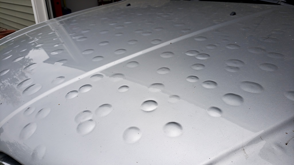 Shallow hail depressions in a dry silver vehicle hood